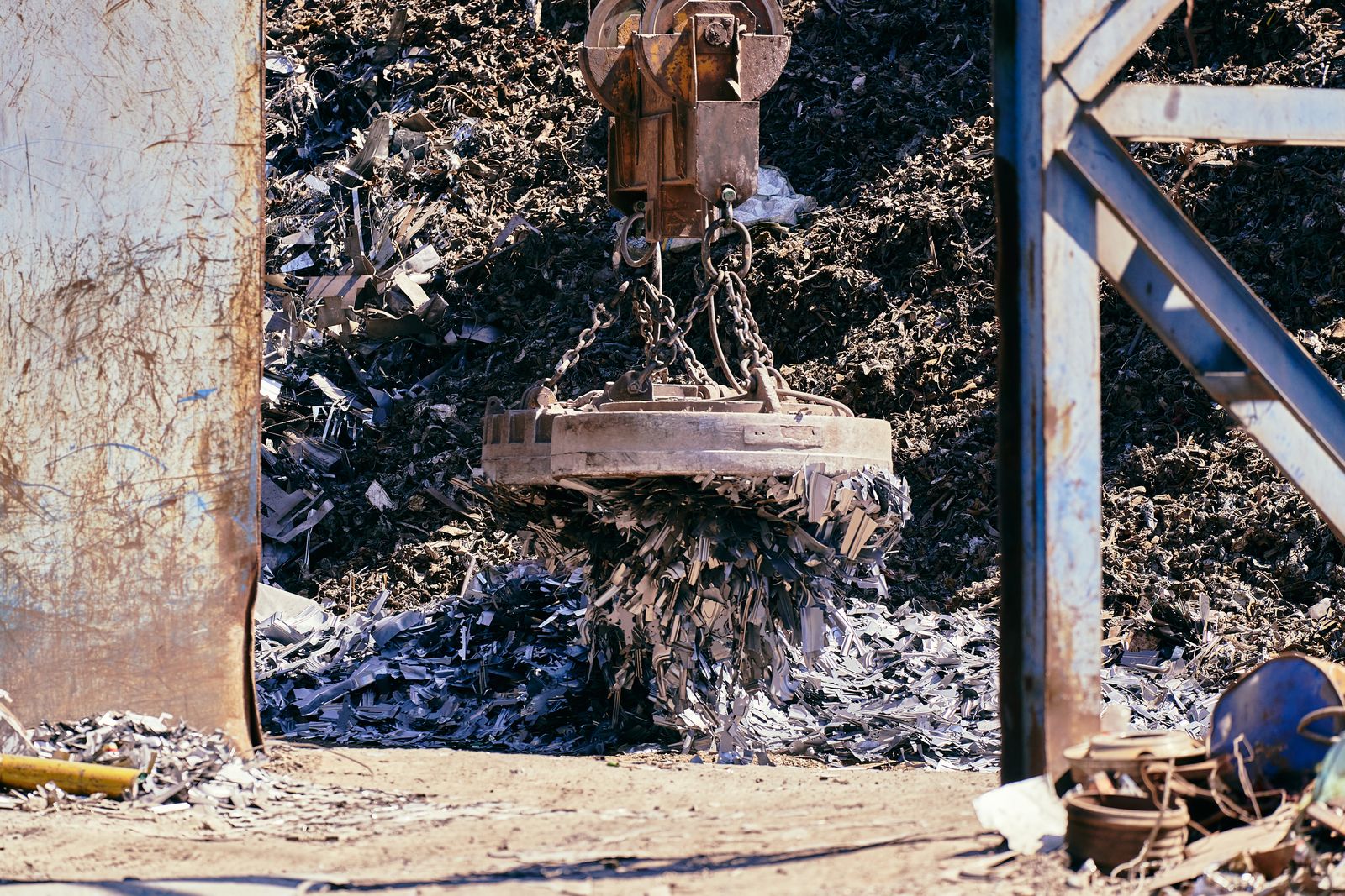 A magnet crane lifting shredded scrap metal in an industrial recycling yard